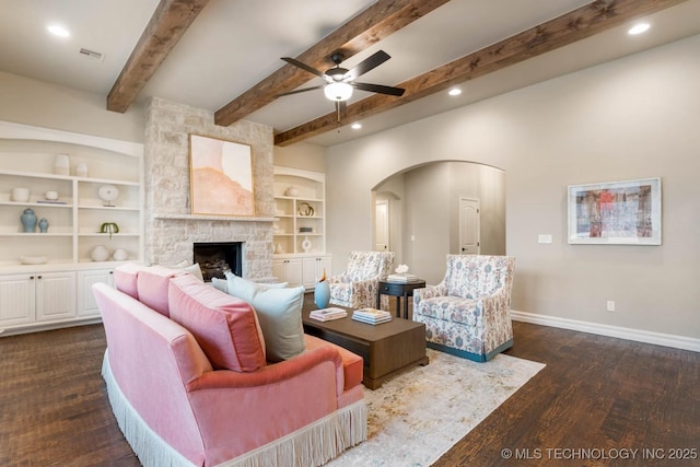 living room featuring dark hardwood / wood-style flooring, built in features, beamed ceiling, ceiling fan, and a fireplace