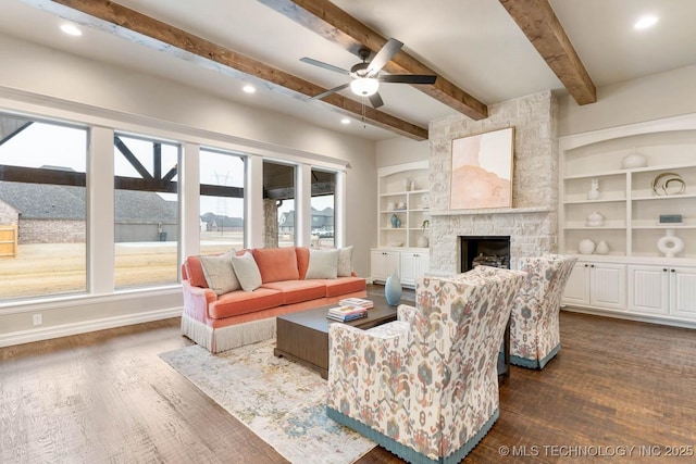 living room with ceiling fan, beam ceiling, dark hardwood / wood-style floors, built in shelves, and a stone fireplace