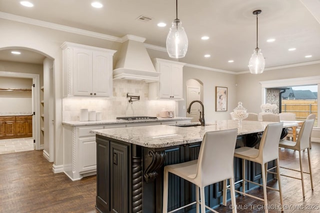 kitchen featuring white cabinetry, sink, custom range hood, and a center island with sink