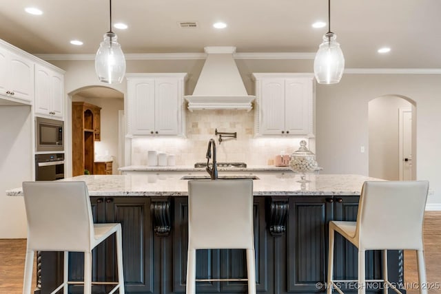 kitchen featuring custom exhaust hood, wood-type flooring, appliances with stainless steel finishes, light stone countertops, and white cabinets