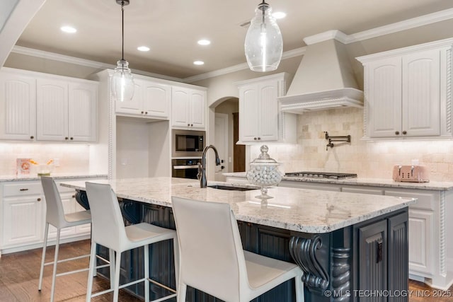 kitchen with sink, white cabinets, a center island with sink, built in microwave, and custom exhaust hood