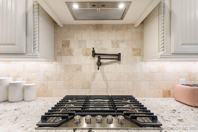 room details with stainless steel gas cooktop, backsplash, white cabinets, and light stone counters