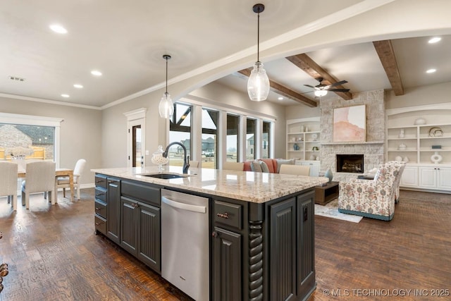 kitchen featuring a stone fireplace, hanging light fixtures, a kitchen island with sink, stainless steel dishwasher, and light stone countertops