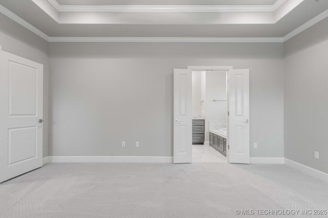 unfurnished bedroom with a raised ceiling, ornamental molding, light carpet, baseboards, and ensuite bathroom