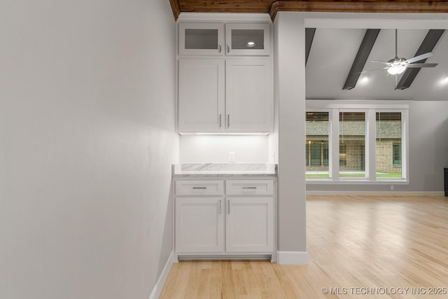 kitchen with light wood finished floors, baseboards, white cabinetry, and light stone counters