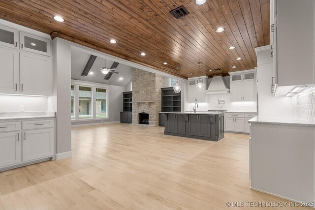 kitchen featuring custom exhaust hood, wooden ceiling, ceiling fan, a sink, and open floor plan