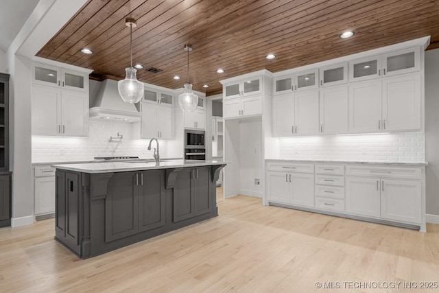 kitchen with wooden ceiling, custom exhaust hood, a sink, white cabinets, and light wood-style floors