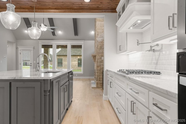 kitchen with gray cabinets, a sink, premium range hood, white cabinets, and backsplash