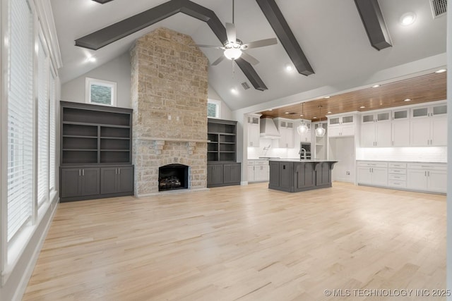 unfurnished living room featuring a sink, a ceiling fan, high vaulted ceiling, light wood-type flooring, and beamed ceiling