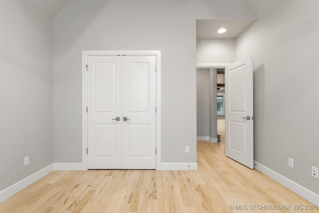 unfurnished bedroom featuring baseboards, light wood-type flooring, a closet, vaulted ceiling, and recessed lighting
