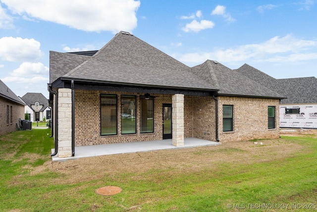 back of house with roof with shingles, a lawn, a patio area, and brick siding