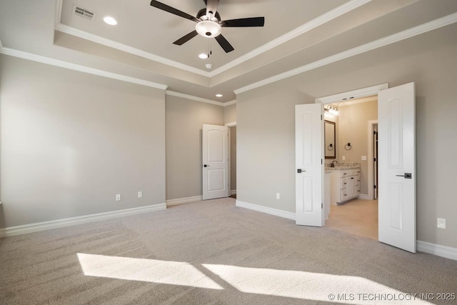 unfurnished bedroom featuring ceiling fan, light colored carpet, a tray ceiling, and ensuite bath