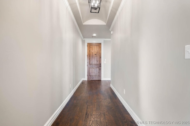 corridor featuring an inviting chandelier, vaulted ceiling, dark wood-type flooring, and crown molding