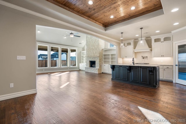 kitchen with white cabinetry, a center island with sink, wooden ceiling, ceiling fan, and custom range hood