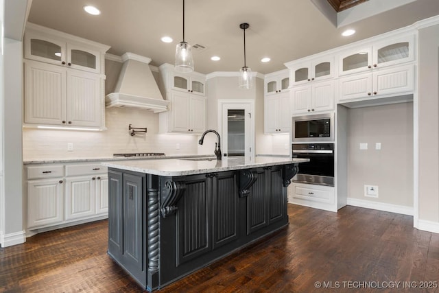 kitchen with premium range hood, white cabinetry, stainless steel oven, and an island with sink