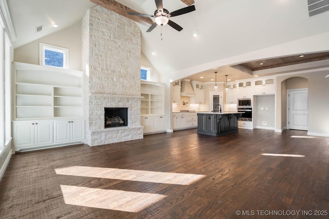 unfurnished living room featuring a stone fireplace, ceiling fan, dark hardwood / wood-style flooring, high vaulted ceiling, and sink