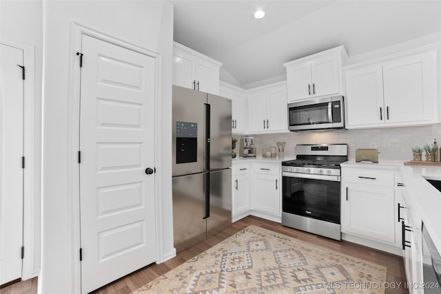 kitchen featuring lofted ceiling, stainless steel appliances, white cabinets, light hardwood / wood-style floors, and backsplash