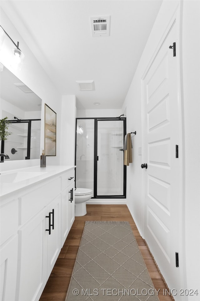 bathroom with hardwood / wood-style flooring, vanity, toilet, and a shower with shower door