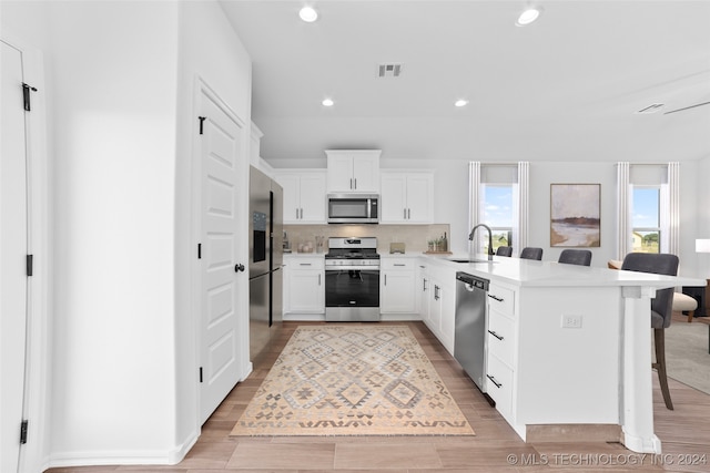 kitchen with stainless steel appliances, sink, light wood-type flooring, and white cabinetry