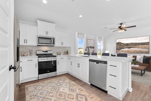 kitchen featuring stainless steel appliances, sink, kitchen peninsula, white cabinetry, and light hardwood / wood-style flooring