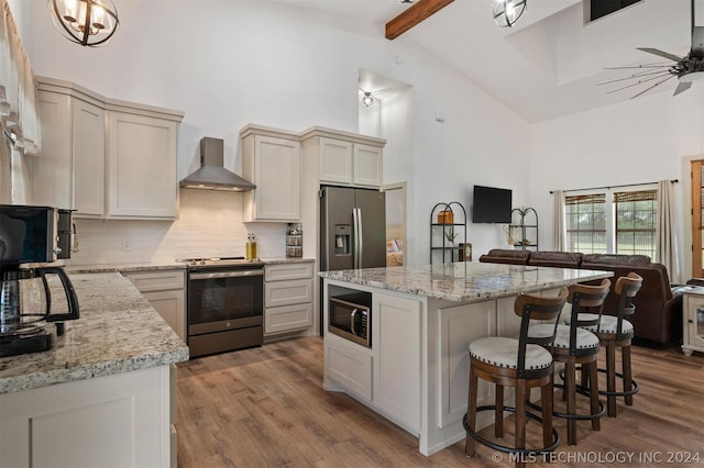 kitchen with light hardwood / wood-style floors, ceiling fan with notable chandelier, stainless steel appliances, and wall chimney exhaust hood