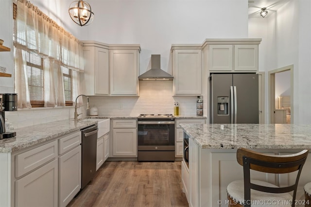 kitchen featuring tasteful backsplash, a chandelier, appliances with stainless steel finishes, wall chimney exhaust hood, and wood-type flooring