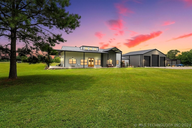 back house at dusk with a garage, a yard, an outdoor structure, and covered porch