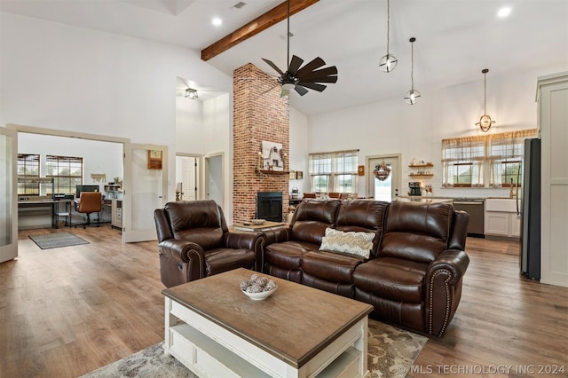 living room with ceiling fan, a fireplace, beamed ceiling, and light hardwood / wood-style flooring