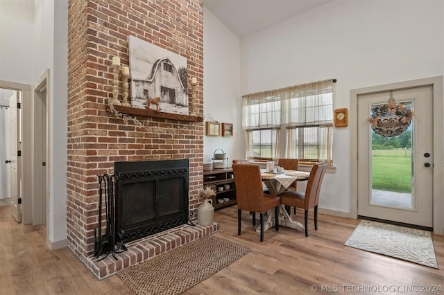 dining area featuring light hardwood / wood-style flooring, a fireplace, a healthy amount of sunlight, and high vaulted ceiling