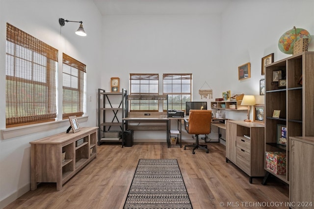 office with light hardwood / wood-style floors, a wealth of natural light, and a high ceiling