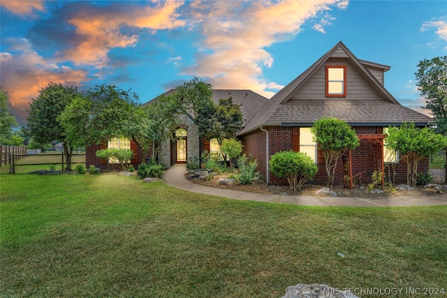 view of front of home with fence, a yard, a shingled roof, and brick siding