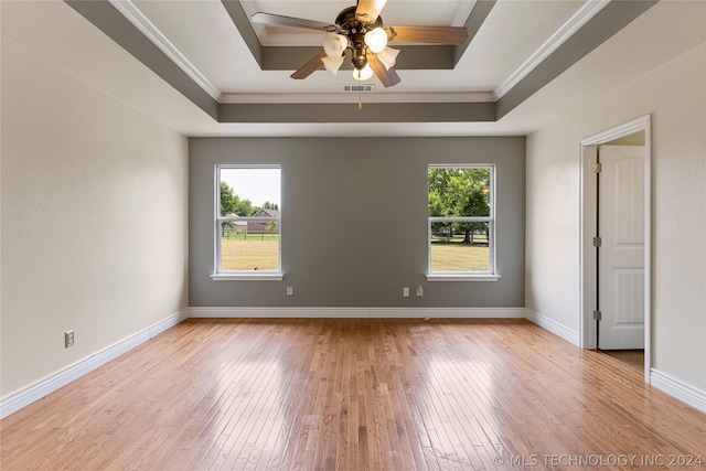 empty room featuring crown molding, a ceiling fan, light wood-style flooring, and a tray ceiling