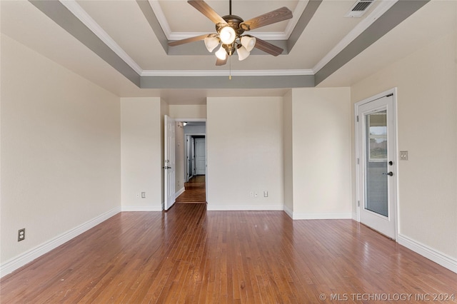 empty room featuring wood-type flooring, a tray ceiling, a ceiling fan, visible vents, and baseboards