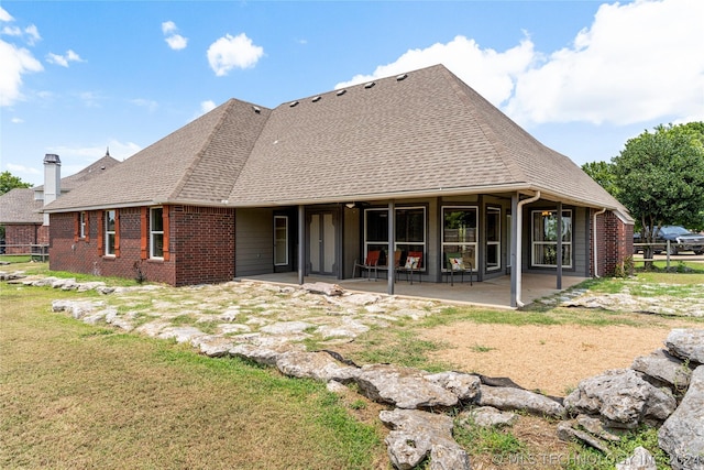 rear view of house with a patio, brick siding, a shingled roof, and a yard
