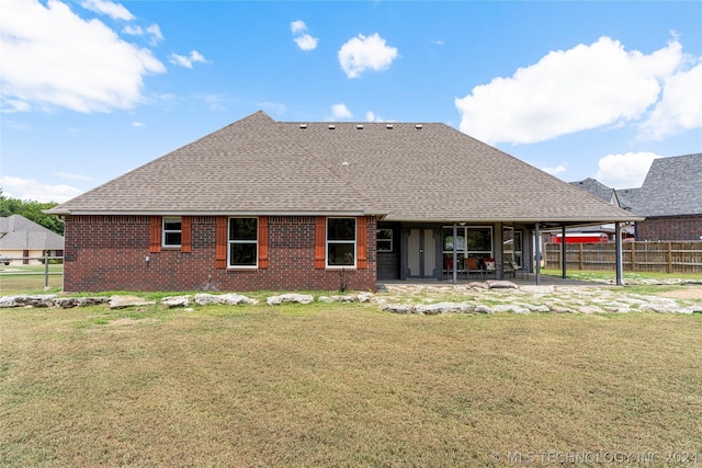 rear view of property featuring a patio, a shingled roof, a lawn, fence, and brick siding