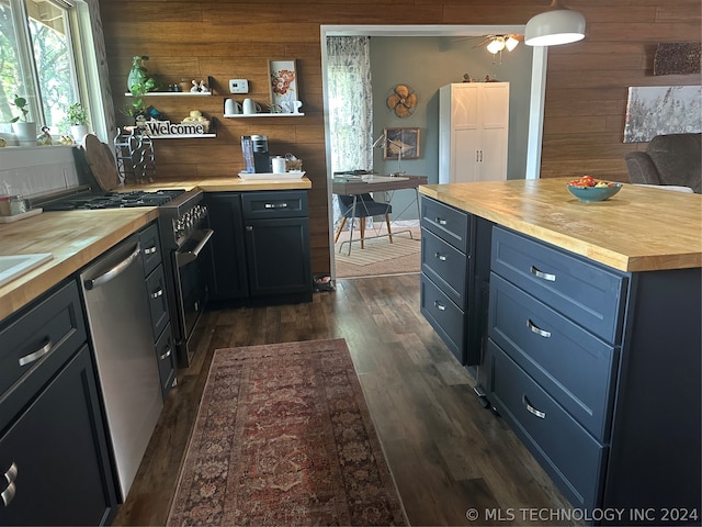 kitchen featuring butcher block countertops, appliances with stainless steel finishes, wood walls, and dark wood-type flooring