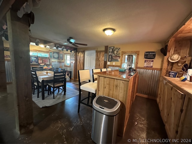 kitchen featuring wooden walls, ceiling fan, and a textured ceiling