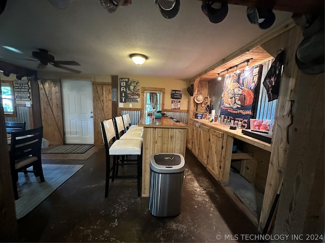 interior space featuring a textured ceiling, wooden walls, ceiling fan, and wooden counters