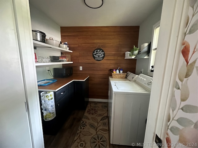 clothes washing area featuring washer and clothes dryer, wood walls, and dark wood-type flooring