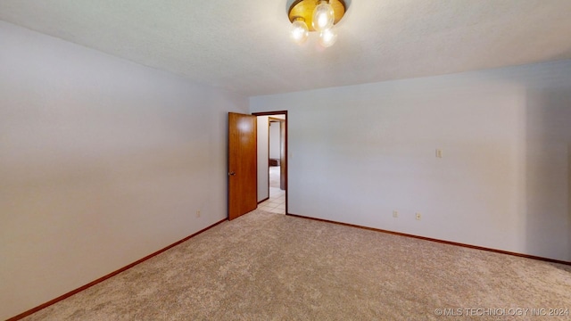 unfurnished room featuring light carpet, a textured ceiling, and baseboards