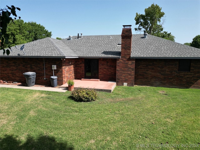 back of house featuring a shingled roof, a lawn, a patio, a chimney, and brick siding