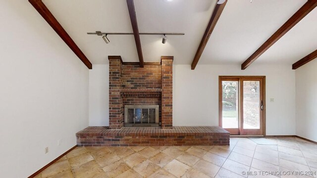 unfurnished living room featuring beamed ceiling, a brick fireplace, and baseboards