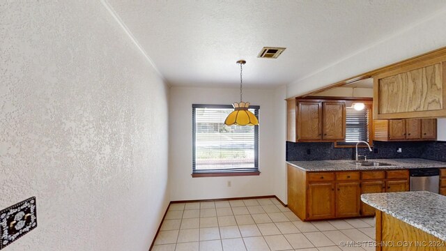 kitchen featuring brown cabinets, decorative light fixtures, a textured wall, stainless steel dishwasher, and a sink