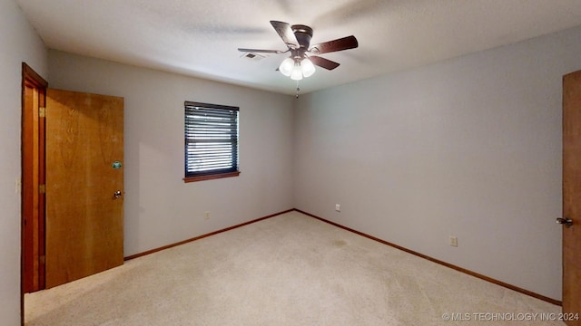 spare room featuring a ceiling fan, light colored carpet, visible vents, and baseboards