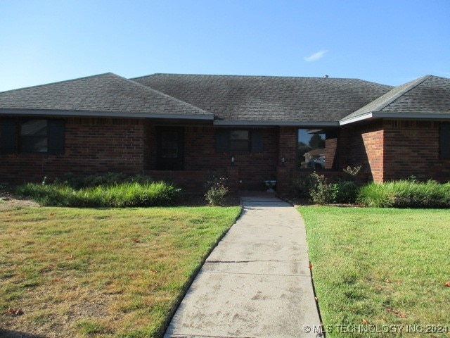 single story home featuring a shingled roof, a front yard, and brick siding