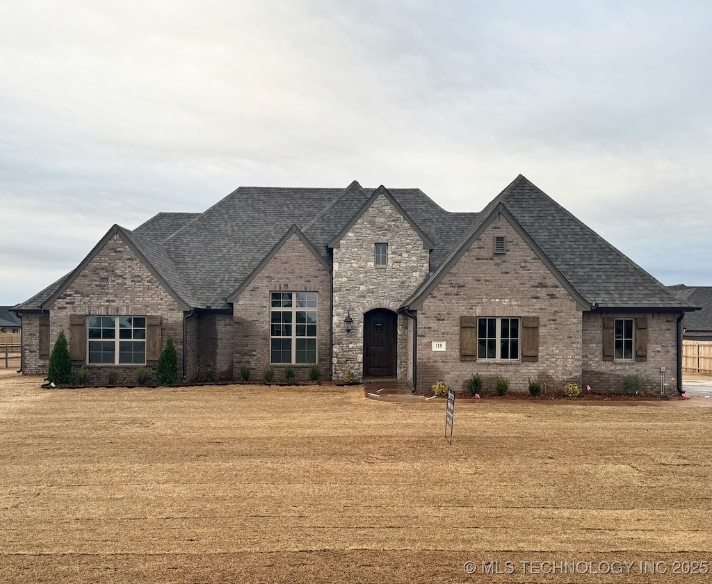 french country inspired facade featuring brick siding, roof with shingles, and a front lawn