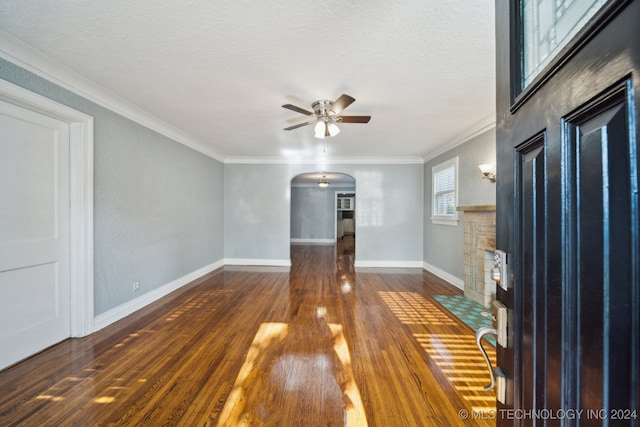 unfurnished living room featuring ceiling fan, a stone fireplace, a textured ceiling, dark wood-type flooring, and crown molding