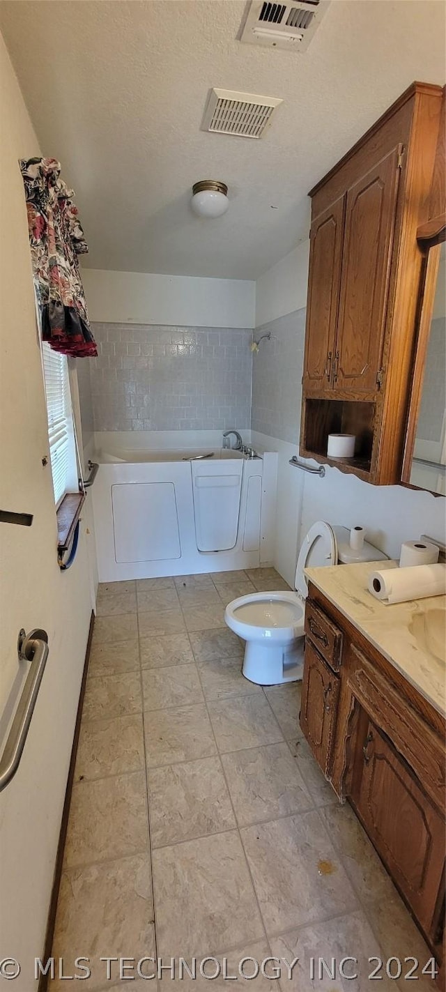 bathroom featuring vanity, a tub to relax in, a textured ceiling, and toilet