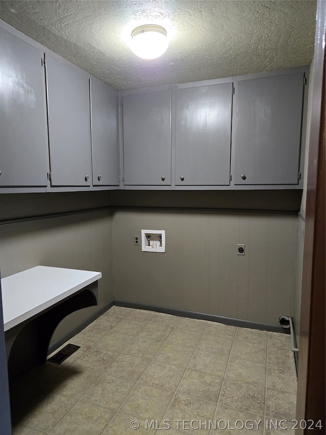 laundry area featuring electric dryer hookup, cabinets, hookup for a washing machine, a textured ceiling, and light tile patterned floors