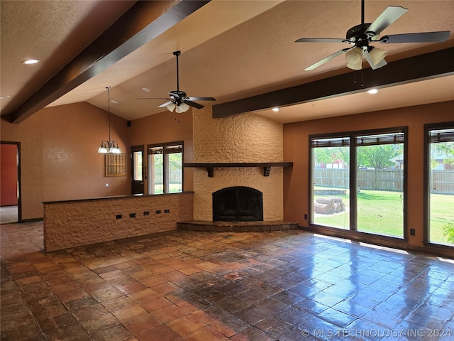 unfurnished living room featuring dark tile patterned floors, ceiling fan with notable chandelier, a stone fireplace, and vaulted ceiling with beams